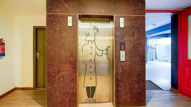 An elevator with a cartoon character on the door, a fire extinguisher on the wall, and a red door to the right. - Spacious Comfort Stays Near Aerospace Museum (Bengaluru)