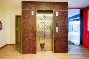 An elevator with a cartoon character on the door, a fire extinguisher on the wall, and a red door to the right. - Spacious Comfort Stays Near Aerospace Museum (Bengaluru)