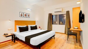 A hotel room with a bed, bedside table, phone, and a desk with a chair. - Spacious Comfort Stays Near Aerospace Museum (Bengaluru)