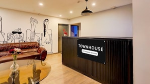 Een receptiegedeelte met een bruine leren bank, een glazen bijzettafeltje met een vaas, en een bordje met de tekst 'TOWNHOUSE Company-Serviced'.