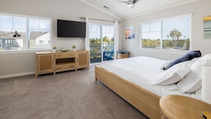 Une chambre à coucher avec un lit, une télévision, un ventilateur de plafond et de grandes fenêtres.