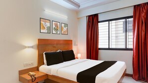 A hotel room with a wooden bed, a nightstand with a phone, and a window with red curtains.