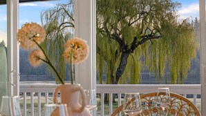 A dining table with a pitcher and glasses, overlooking a lake with weeping willow trees. - 3B2B Upper Unit w/ Oceanfront & Rainier Views (Bremerton)