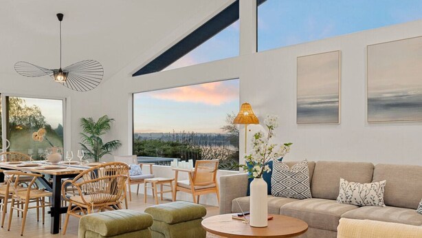 A spacious living area with a large window offering a scenic view, a dining area with wicker furniture, and a cozy seating arrangement with a sofa and ottomans. - 3B2B Upper Unit w/ Oceanfront & Rainier Views (Bremerton)