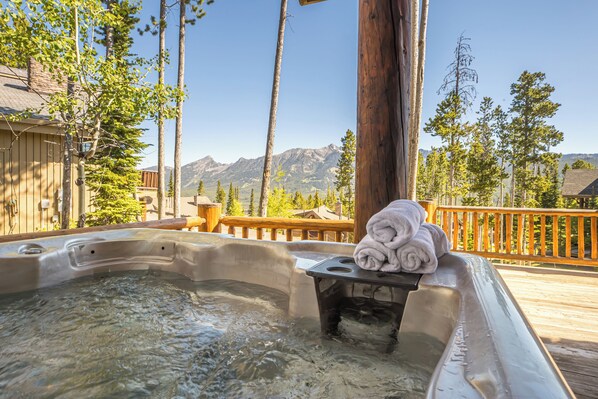 A hot tub with a wooden deck, surrounded by trees and mountains in the background.