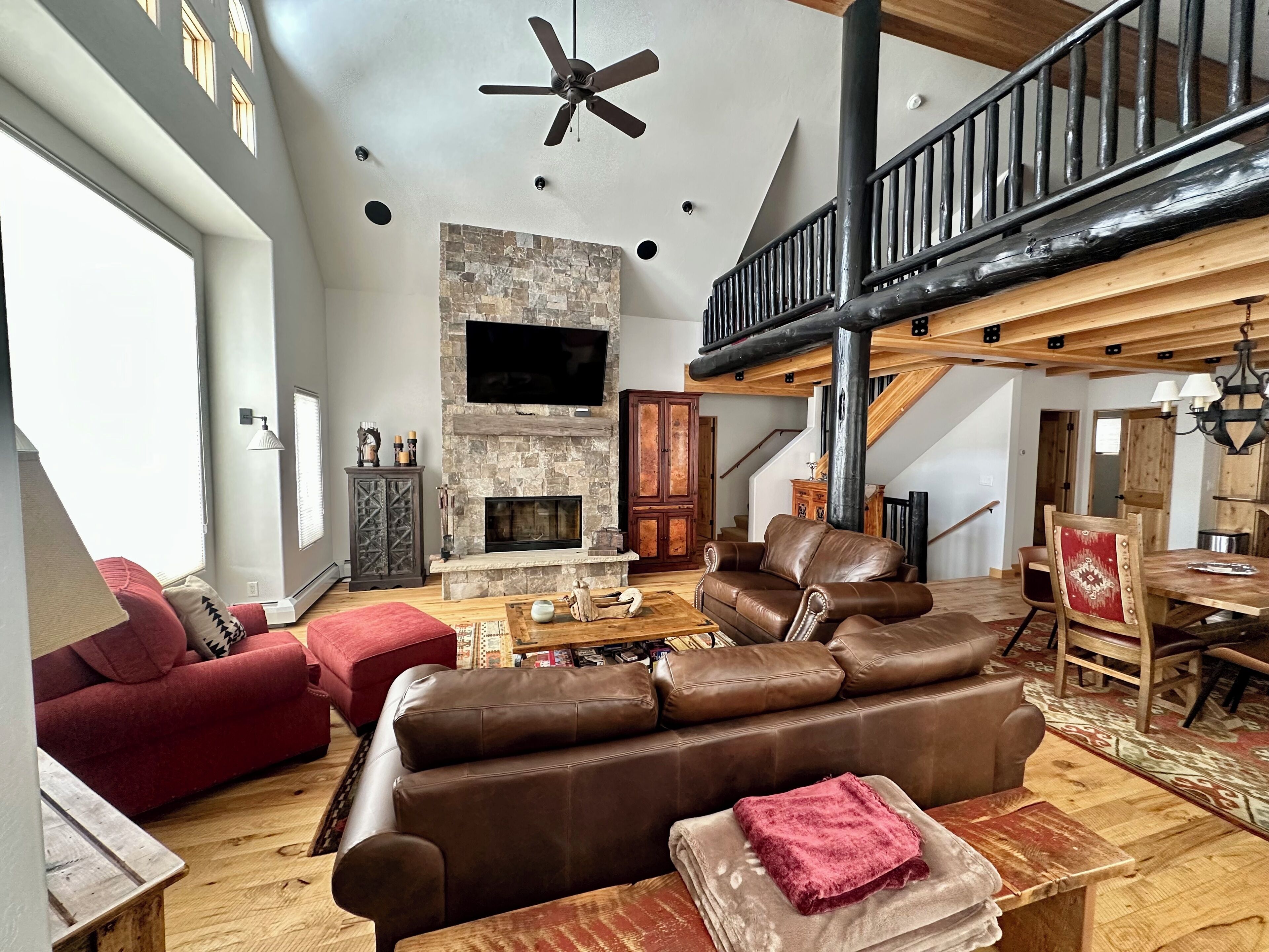 A spacious living room with a fireplace, leather sofas, and a high ceiling fan.