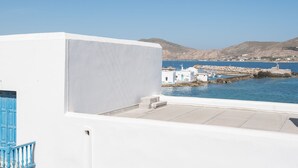 A white building with a blue door, a balcony, and a view of a coastal area with white buildings and a blue sea. - Seaview House 2 From the Town (Paros)