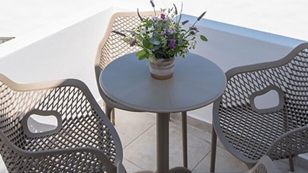 A terrace with a round table and two chairs, a potted plant, and a view of the sea and distant hills. - Seaview House 2 From the Town (Paros)