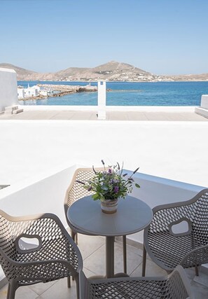 Una terraza con una mesa redonda y dos sillas, una planta en maceta y vistas al mar y colinas distantes.