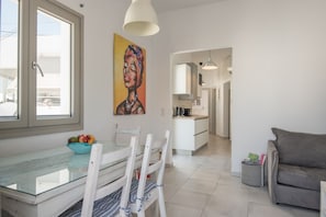Eine moderne Küche mit weißen Schränken, ein Essbereich mit einem Glastisch und ein graues Sofa.