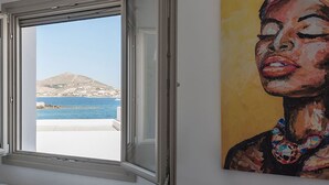 A room with a window overlooking a coastal view, a painting on the wall, and a white radiator. - Seaview House 2 From the Town (Paros)