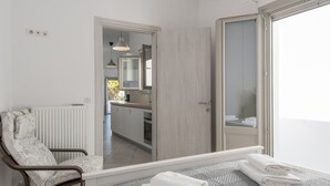 A modern bathroom with a shower, a toilet, and a sink. There is a chair with a floral pattern and a towel rack with folded towels. - Seaview House 2 From the Town (Paros)