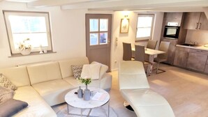 Ein modernes Wohnzimmer mit einer Couch, einem Relaxsessel, einem Couchtisch und einer Küchenzeile mit Schränken und einem Herd.