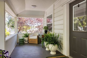 A covered porch with a wicker chair, potted plants, and a view of autumn trees. - Stylish Retreat. Grand Private Yard. Fire Pit. A/C (Napa)
