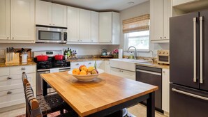A modern kitchen with white cabinets, stainless steel appliances, a wooden dining table with a fruit bowl, and a black refrigerator. - Stylish Retreat. Grand Private Yard. Fire Pit. A/C (Napa)