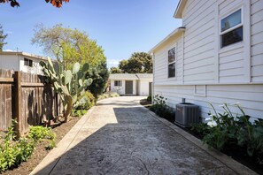 A residential driveway leading to a house with a wooden fence, a cactus, and a garden.