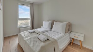 A bedroom with a bed, a bedside table, and a window with a view of the landscape. - Horizon 133 - SeaView by GrandApartments (Gdansk)