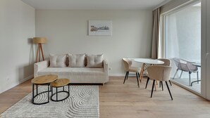 A modern living room with a sofa, two wooden tables, a floor lamp, and a view through a large window. - Horizon 133 - SeaView by GrandApartments (Gdansk)