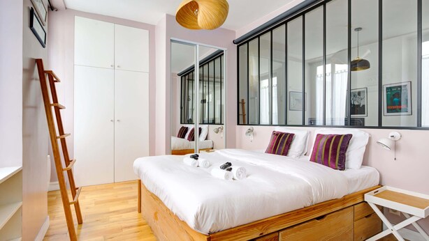 A bedroom with a wooden bed, white bedding, a ladder, a white desk, and a large window with blinds. - Lumunous apartment - 1BDR/5P au coeur du Marais (Paris)