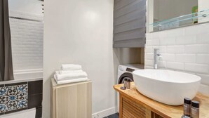 A modern bathroom with a large oval sink, a glass shower enclosure, a built-in washing machine, and a wooden vanity. - Lumunous apartment - 1BDR/5P au coeur du Marais (Paris)