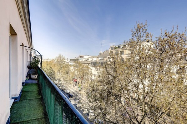 A balcony with a green mat, a potted plant, and a view of buildings and trees.
