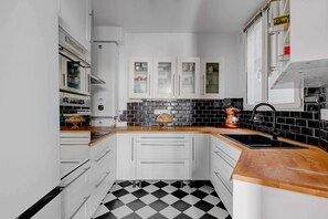 A kitchen with white cabinets, a black and white checkered floor, and a wooden countertop.