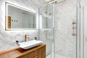 A bathroom with a glass-enclosed shower, a large mirror, and a wooden vanity with a vessel sink.