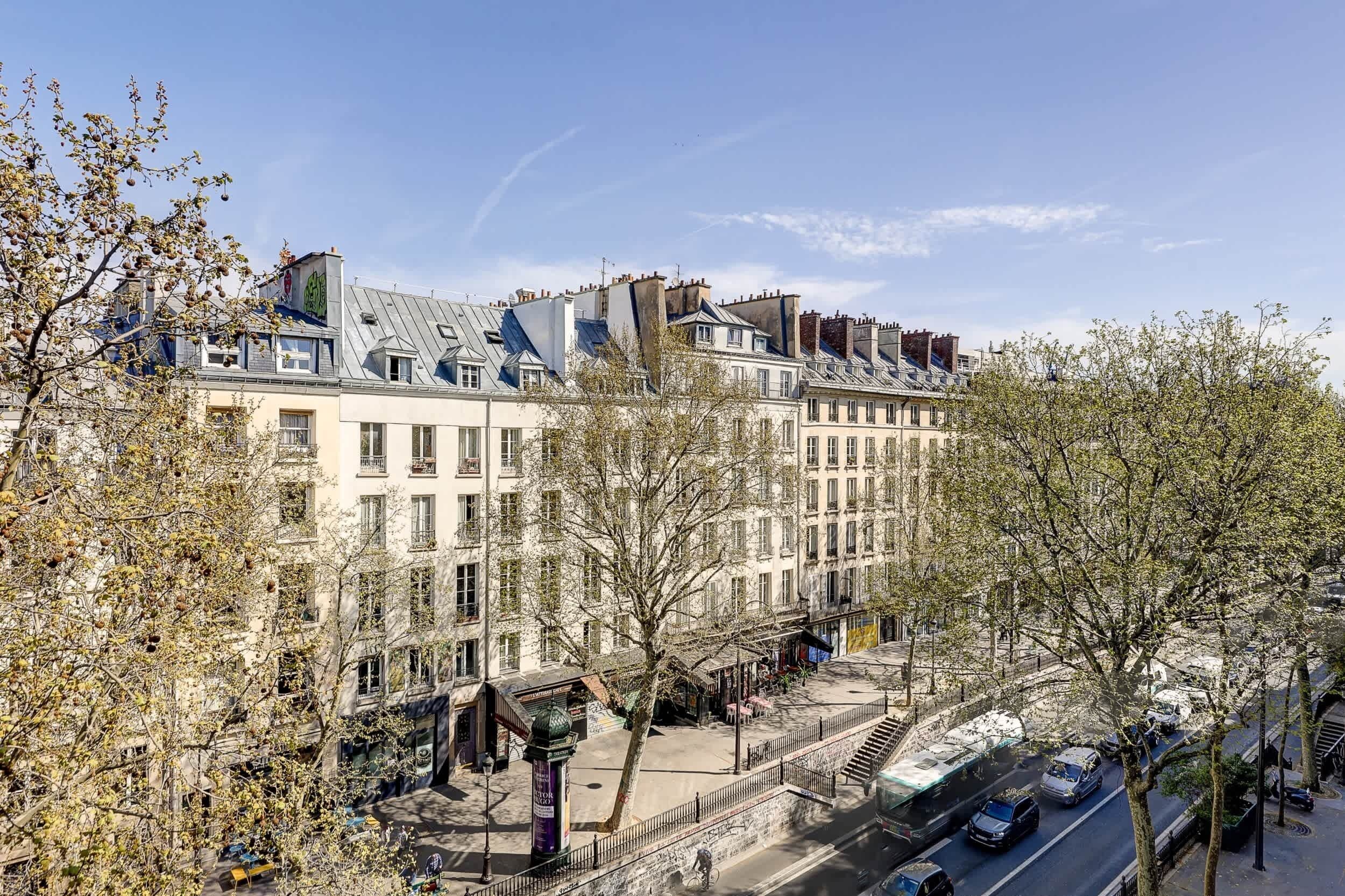 A row of traditional European buildings with a central pedestrian area and a street with parked cars.
