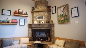 A cozy living room with a stone fireplace, wooden ceiling, and a couch with cushions. - Plis Bujtina (Margegaj)