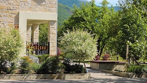 A stone building with a balcony and a garden with various plants and trees. - Plis Bujtina (Margegaj)