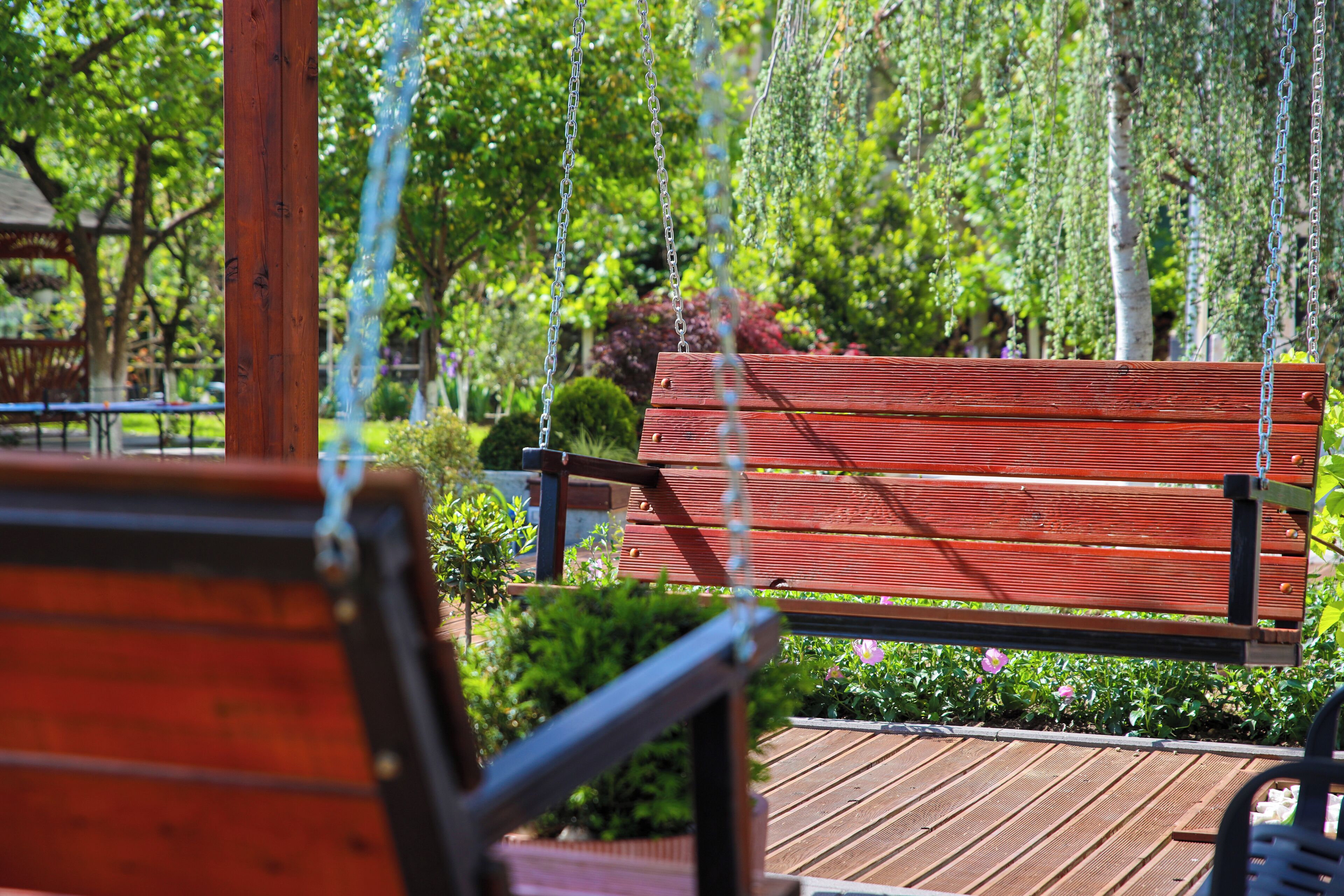 A wooden bench in a park with a wooden deck and greenery in the background.