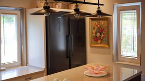 A kitchen with a central island, a refrigerator, and pendant lighting. - Plis Bujtina (Margegaj)