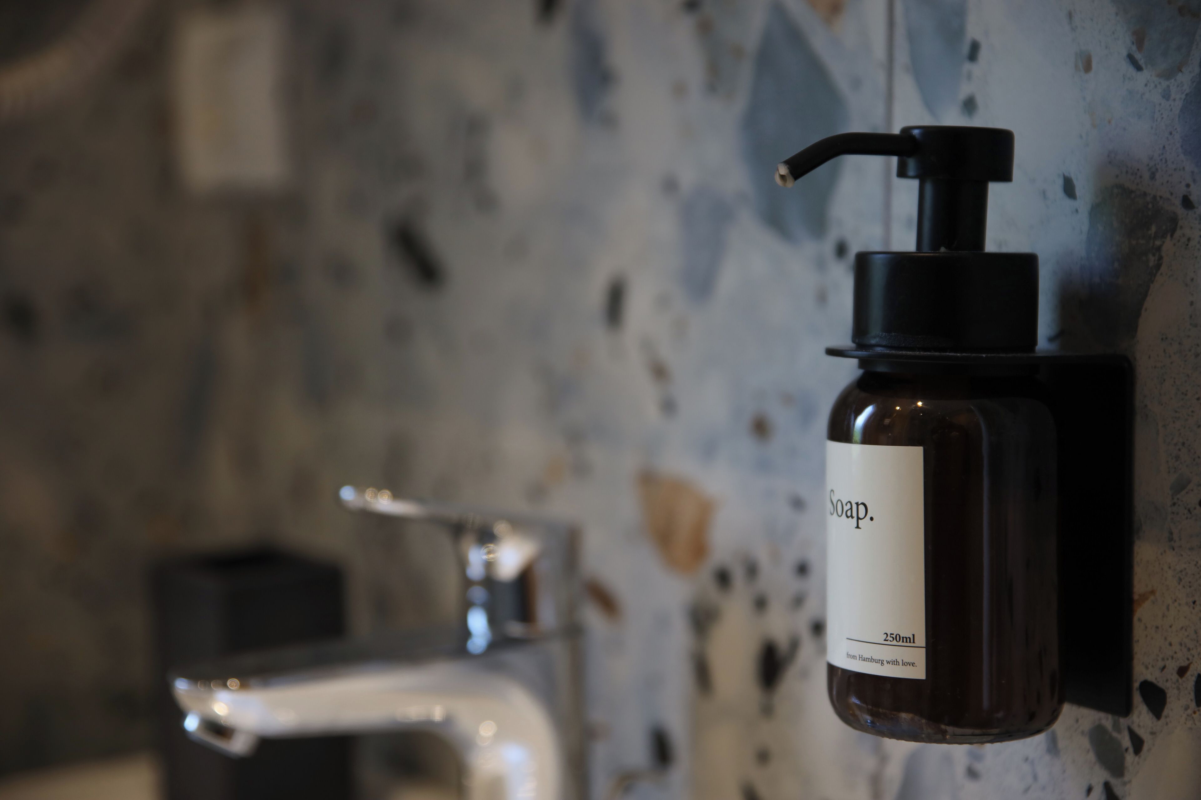 A bathroom with a soap dispenser mounted on the wall and a faucet.