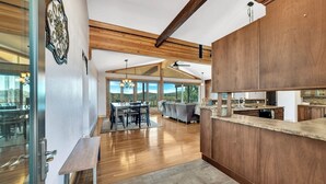 A modern kitchen with wooden cabinets, a dining area with a large table and chairs, and a view of the outdoors. - Whiskey Mountain- What a view! (Lead)