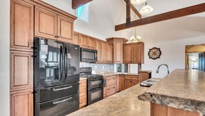 A kitchen with wooden cabinets, a black refrigerator, a stove, and a granite countertop. - Whiskey Mountain- What a view! (Lead)