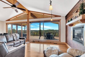 A spacious living room with a large sliding glass door leading to an outdoor deck, a ceiling fan, and a fireplace. - Whiskey Mountain- What a view! (Lead)
