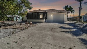 A single-story house with a garage, surrounded by trees and a gravel driveway.