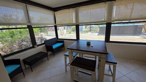 A sunroom with a table and benches, large windows with blinds, and a view of the outside.