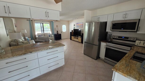 A modern kitchen with stainless steel appliances, a dining area with a marble countertop, and a living room with a sofa and TV.