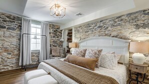 Un dormitorio con pared de piedra, una cama con cabecera, una mesita de noche y una lámpara colgante.