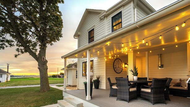 Una casa con porche cubierto, mobiliario exterior y luces colgantes.