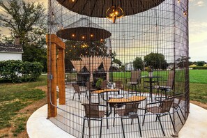 Un patio exterior con mesas y sillas, rodeado por una cerca metálica y un techo decorativo.