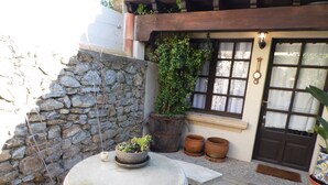 Un muro de piedra, una planta en maceta, una mesa redonda y una puerta con ventanal.