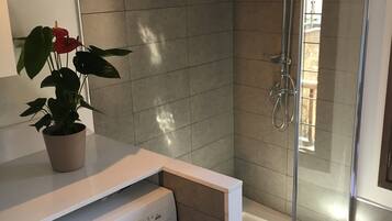 A compact bathroom with a washing machine, a glass shower enclosure, and a potted plant.