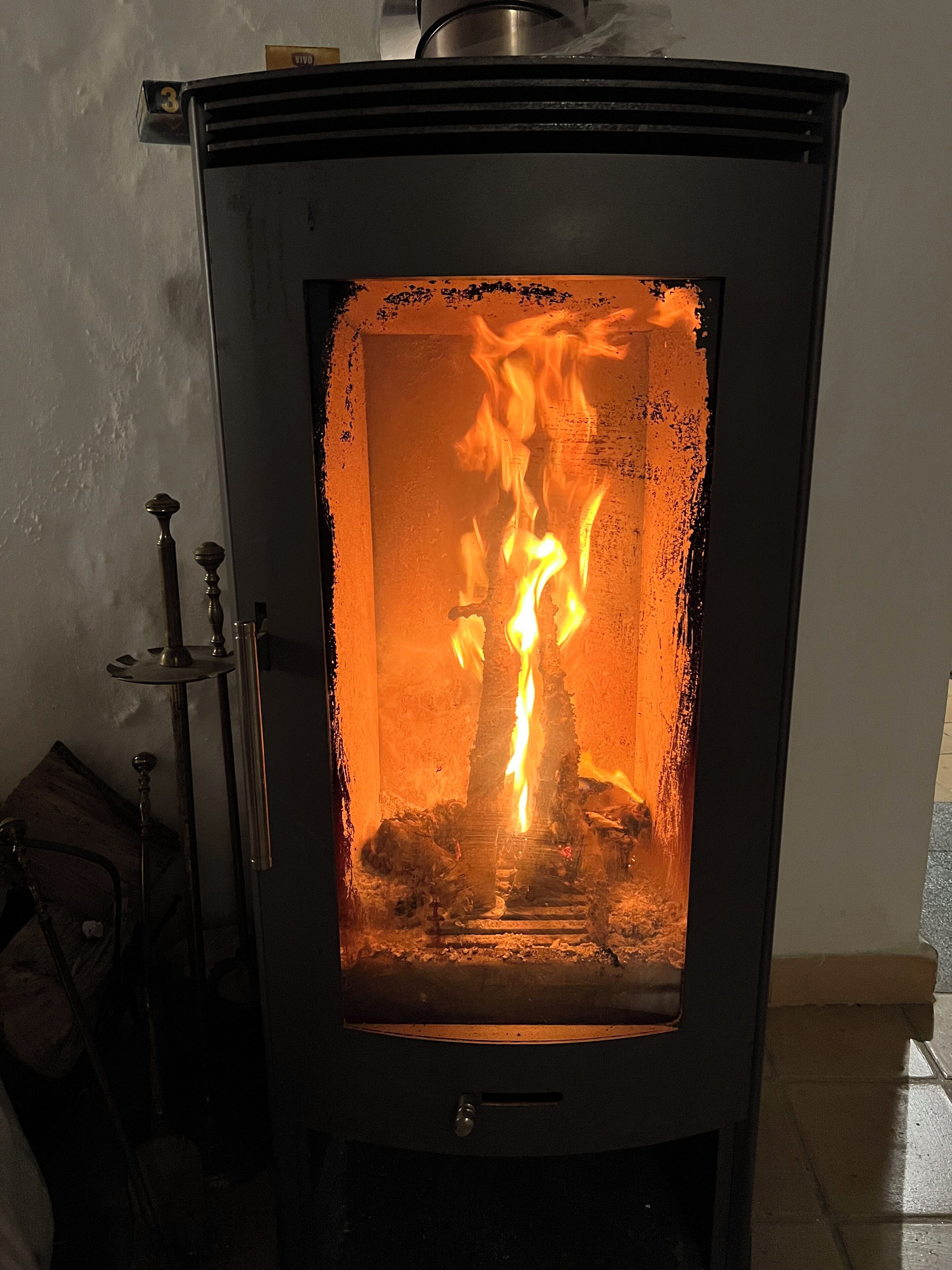A wood-burning stove with visible flames inside, a metal handle, and a small shelf at the top.