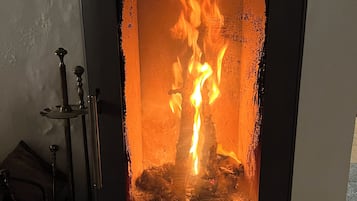 A wood-burning stove with visible flames inside, a metal handle, and a small shelf at the top.