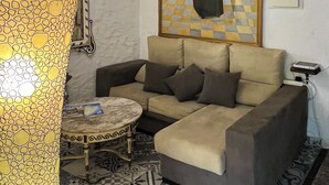 Una sala de estar con un sofá, una mesa redonda de centro, una lámpara estampada, un espejo grande y un cuadro en la pared.