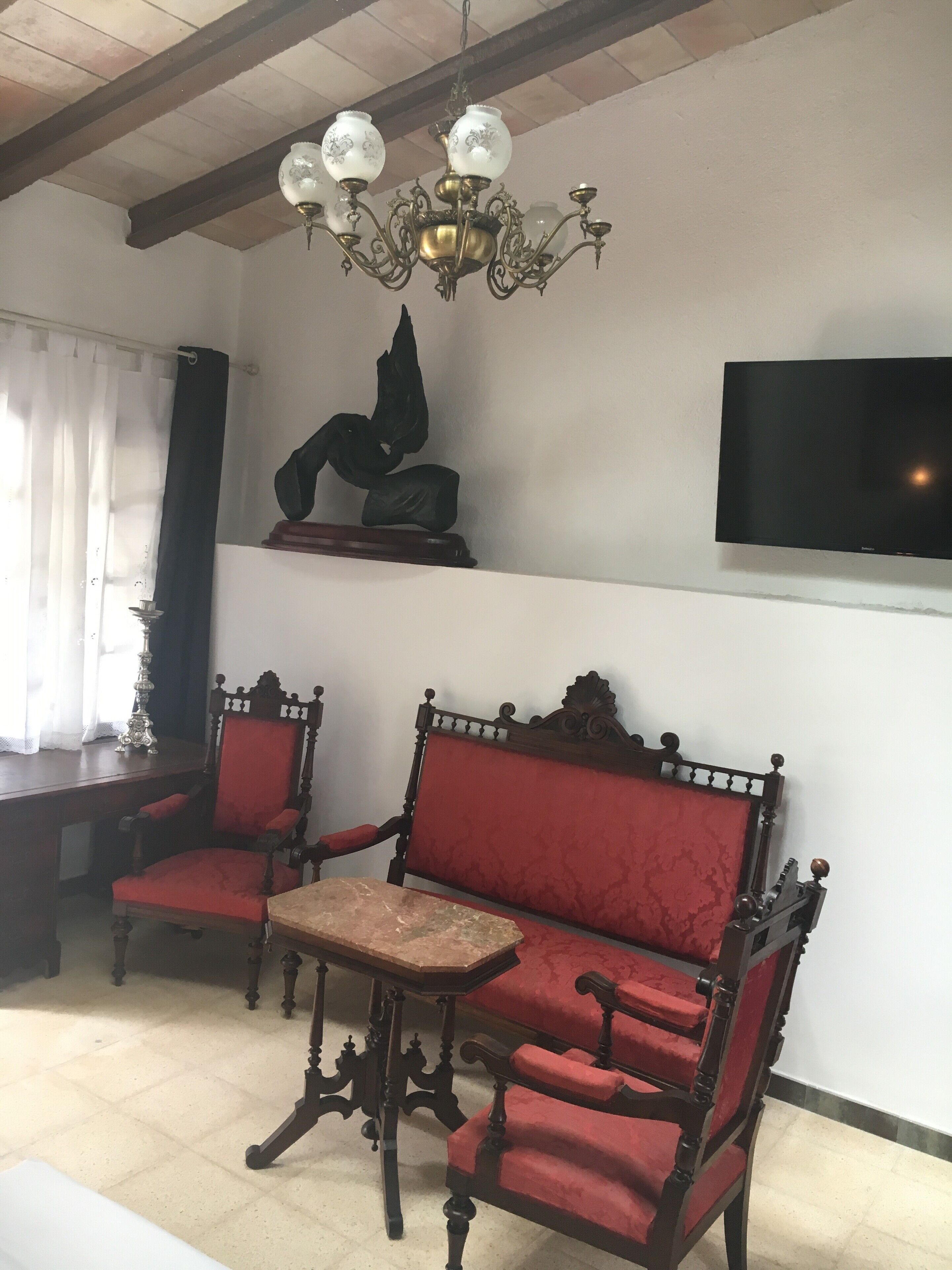 Ein Zimmer mit einer Chandelier, einem an der Wand montierten Fernseher und zwei roten, gepolsterten Sesseln sowie einem kleinen Tisch in der Mitte.