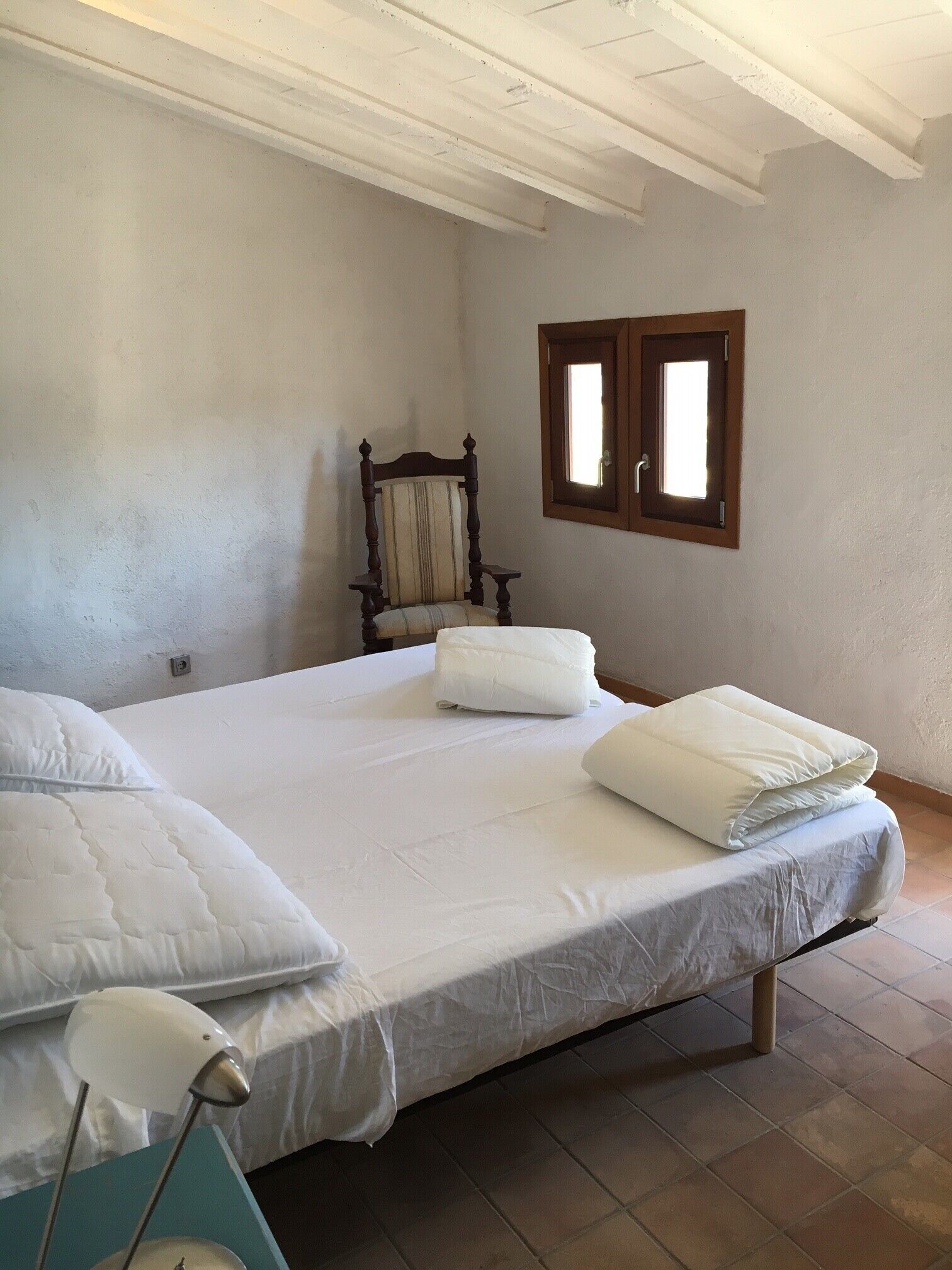 Une chambre à coucher avec un lit, des oreillers, une chaise, une fenêtre et une lampe.