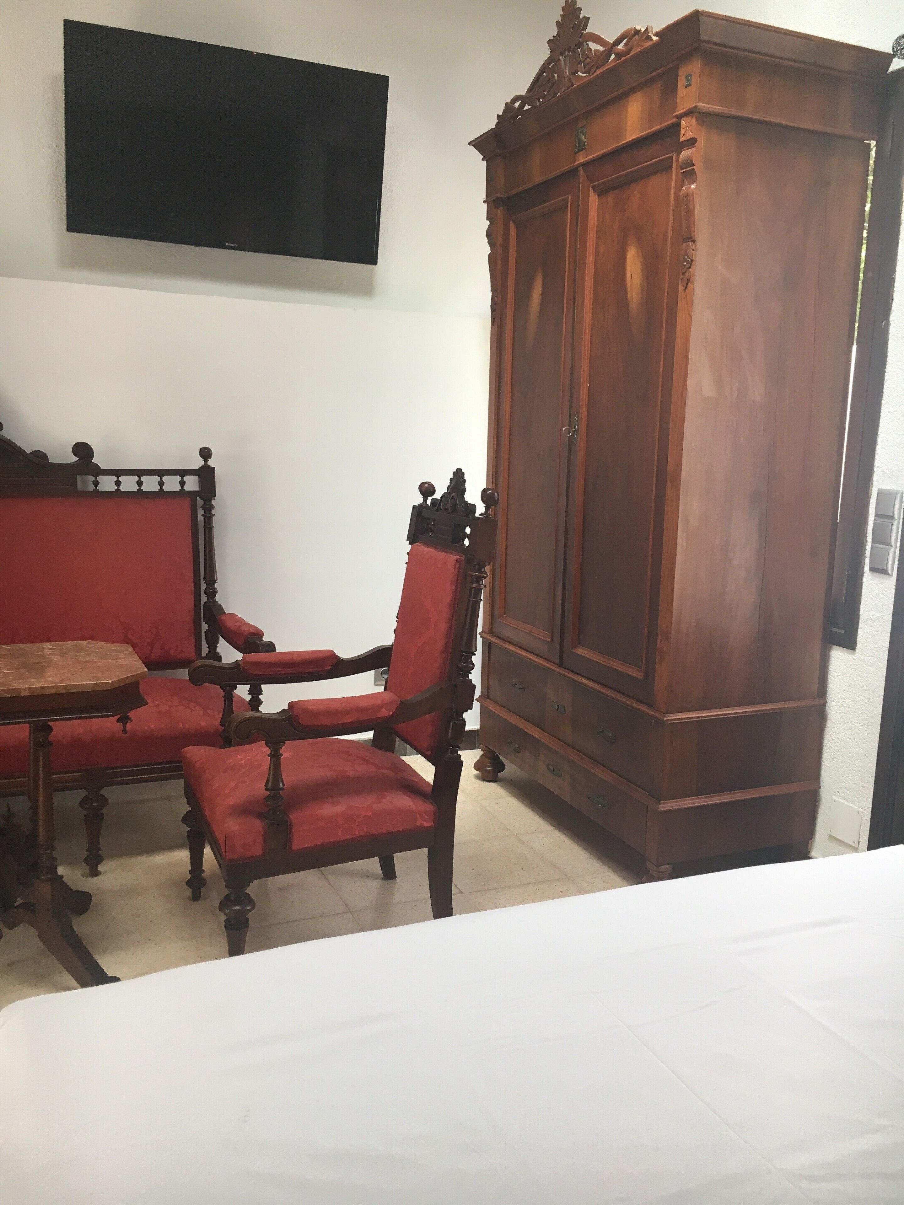 Ein Zimmer mit einem Bett, einem Holzschrank, einem roten Sessel und einem an der Wand befestigten Fernseher.